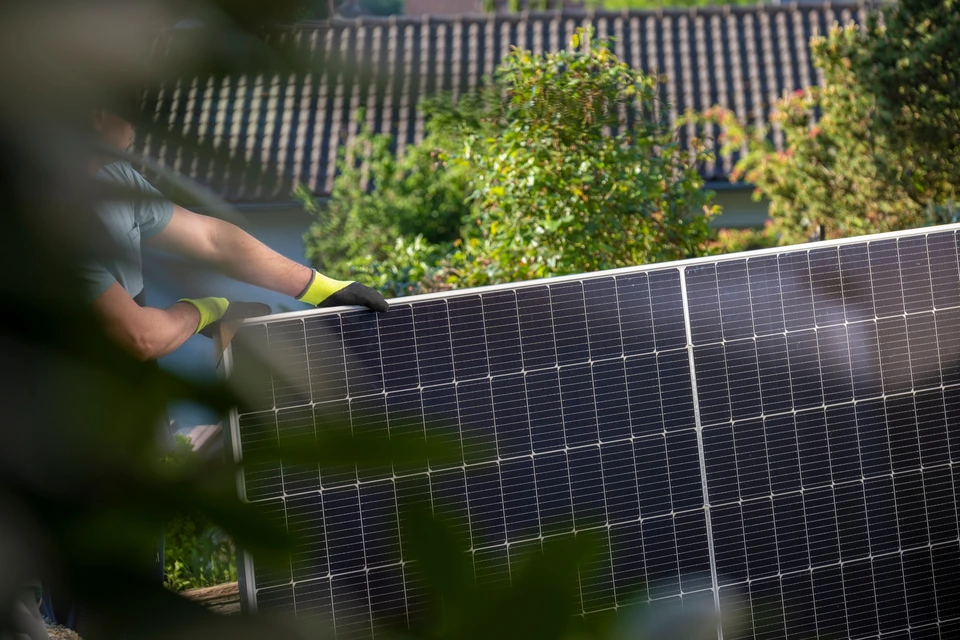 Technicien installant des panneaux solaires photovoltaïques sur toiture résidentielle sous ciel bleu